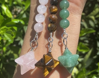 May include: Three crystal star pendants on silver chains. The stars are made of rose quartz, tiger's eye, and green aventurine. Each star is attached to a strand of beads made of the same crystal.