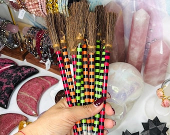 May include: A collection of pencils topped with brown bristles resembling miniature broomsticks. The pencil barrels feature alternating horizontal stripes in bright neon pink, lime green, and orange colors, with clear plastic tips at the base.