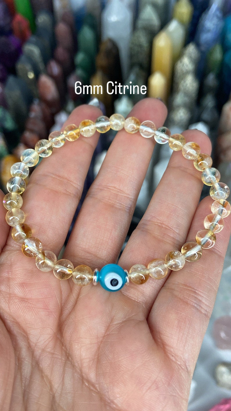 K&ouml;nnte beinhalten: Ein Armband aus 6 mm Citrinperlen mit einem blauen b&ouml;sen Blick-Anh&auml;nger.