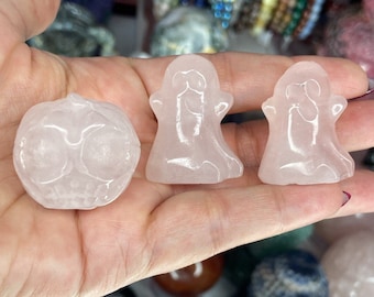 May include: Three small, pale pink, translucent carved stone figurines. One figurine is shaped like a round pumpkin with carved facial features, and two figurines are shaped like ghosts with smooth, rounded forms and polished surfaces.
