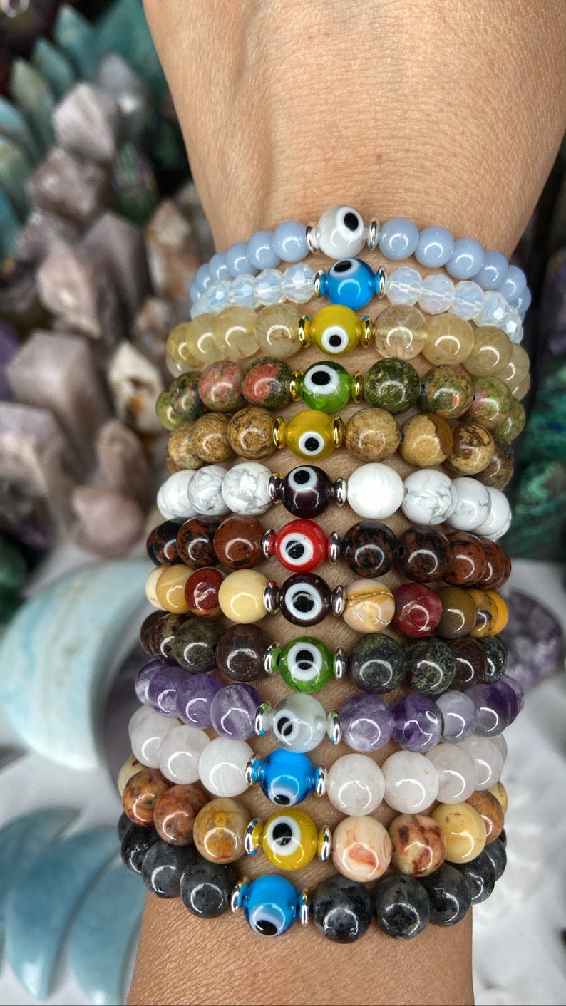 K&ouml;nnte beinhalten: Ein Stapel Armb&auml;nder mit verschiedenen farbigen Perlen und b&ouml;sen Augen-Anh&auml;ngern. Die Armb&auml;nder sind aus verschiedenen Materialien gefertigt, darunter Stein, Glas und Metall. Die b&ouml;sen Augen-Anh&auml;nger sind alle in verschiedenen Farben und Designs gehalten.