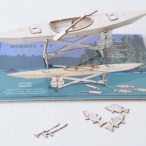 May include: A wooden model kit of a kayak with a paddle, life vest, bilge pump, and fishing pole. The kit includes illustrated instructions and is made in Portland, Oregon.