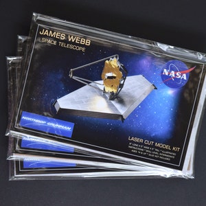 May include: Three packages of a laser cut model kit of the James Webb Space Telescope. The model is 8 inches long, 5 inches wide, and 5 inches tall. The packaging features a photo of the telescope and the NASA logo. The kit is for ages 14 and up and requires glue, which is not included.