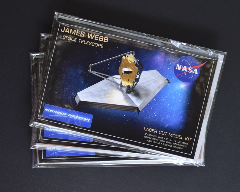 May include: Three packages of a laser cut model kit of the James Webb Space Telescope. The model is 8 inches long, 5 inches wide, and 5 inches tall. The packaging features a photo of the telescope and the NASA logo. The kit is for ages 14 and up and requires glue, which is not included.