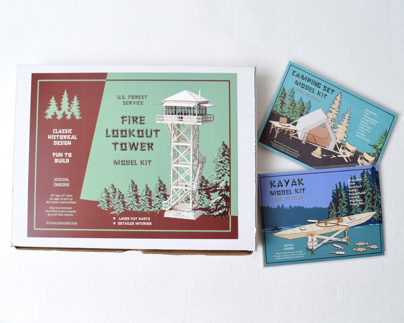 May include: A white box with a red and green design featuring a model kit of a fire lookout tower. The box includes the text "U.S. Forest Service Fire Lookout Tower Model Kit".  The box is next to two smaller boxes, one blue and one green, with model kits of a kayak and a camping set.