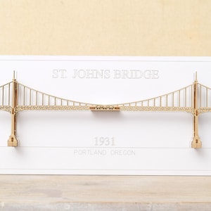 May include: A white card with a laser-cut wooden model of the St. Johns Bridge in Portland, Oregon. The card features the text "St. Johns Bridge" and "1931" with the city and state below.