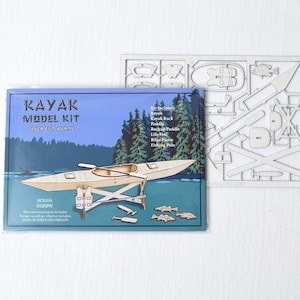 May include: A laser-cut wooden model kit of a kayak with a paddle, life vest, and fishing pole. The kit includes instructions and is made in Portland, Oregon.