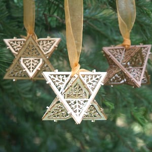 May include: Three wooden star-shaped ornaments with intricate snowflake designs. Each ornament is suspended from a gold ribbon.