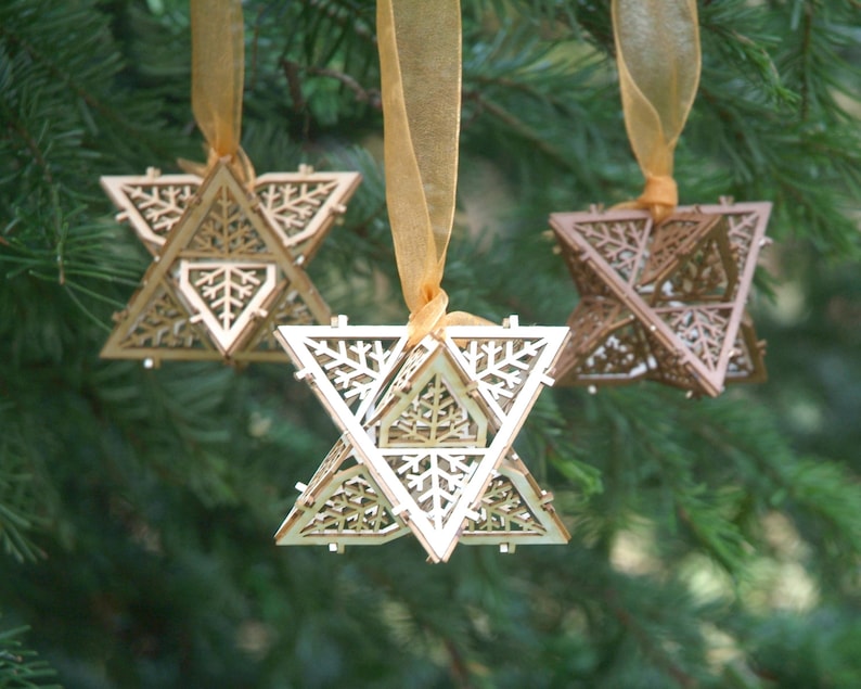 May include: Three wooden star-shaped ornaments with intricate snowflake designs. Each ornament is suspended from a gold ribbon.