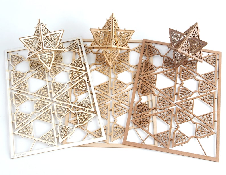May include: Three unfinished wooden star-shaped ornaments with intricate laser-cut designs. The ornaments are layered on top of each other, with the largest ornament at the bottom and the smallest ornament at the top. The ornaments are made of light brown wood.