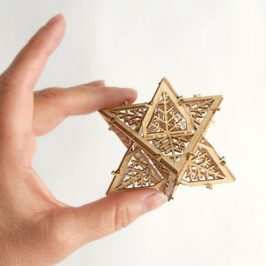 May include: A wooden geometric star ornament with a intricate, lacy design. The star is made of multiple pieces of wood that are joined together to create a three-dimensional shape.