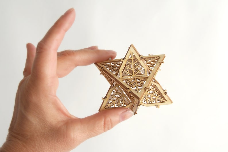 May include: A wooden geometric star ornament with a intricate, lacy design. The star is made of multiple pieces of wood that are joined together to create a three-dimensional shape.