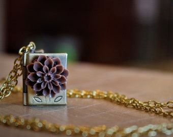 Gold book locket necklace with purple flower, and gold coloured chain.