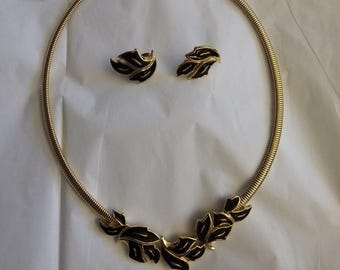 May include: A gold necklace with a black leaf design and matching earrings. The necklace is a simple chain with a delicate leaf design. The earrings are small and feature a single leaf.