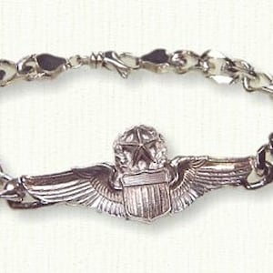 May include: A silver bracelet with a silver charm in the shape of an Air Force pilot's wings. The charm features a star and a shield with a stylized American flag.