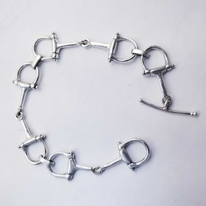 May include: Silver bracelet made of linked horse bit charms. The bracelet has a hook and eye clasp.