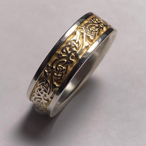 May include: A silver band ring with a gold Celtic knot design.