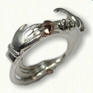 May include: A silver ring featuring two hands holding a heart. The heart is made of rose gold.