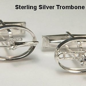 Può includere: Gemelli a trombone in argento sterling. I gemelli presentano un design a trombone all'interno di una cornice ovale. Il testo "Sterling Silver Trombone Cuff Links" è in alto e "raru.com" in basso.