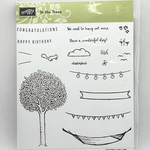May include: A clear plastic case containing a rubber stamp set with nature-themed designs. Includes a tree, squirrel, cloud, grass, string lights, banner, and hammock. Text includes "In the Trees", "Congratulations", and "Happy Birthday".