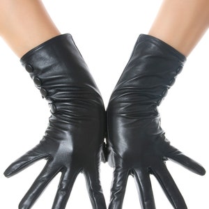 Könnte beinhalten: Ein Paar schwarze Lederhandschuhe mit Knopfdetails am Handgelenk. Die Handschuhe sind lang, reichen über das Handgelenk hinaus und haben eine glatte, glänzende Oberfläche. Die Finger sind vollständig ausgestreckt.