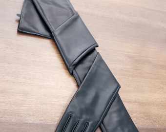 May include: A pair of long black leather gloves. The gloves are folded in half and the fingertips are visible.