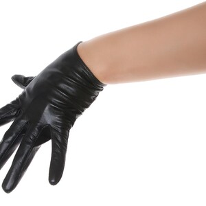 May include: A black leather glove with a smooth, slightly shiny finish and subtle horizontal folds around the wrist area. The glove features stitched seams along the fingers and palm, extending to cover the hand and wrist with a fitted design.