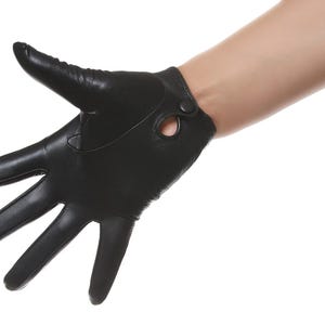 May include: A black leather glove featuring a smooth finish, five individual finger sections, and a small circular cutout detail near the wrist area secured with a single matching black snap button closure for a secure fit around the hand.