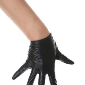 May include: A short black leather glove with a smooth finish and visible stitching along the fingers. The glove features a slightly gathered wrist area and extends to cover the palm and fingers, providing a sleek and fitted appearance on the hand.