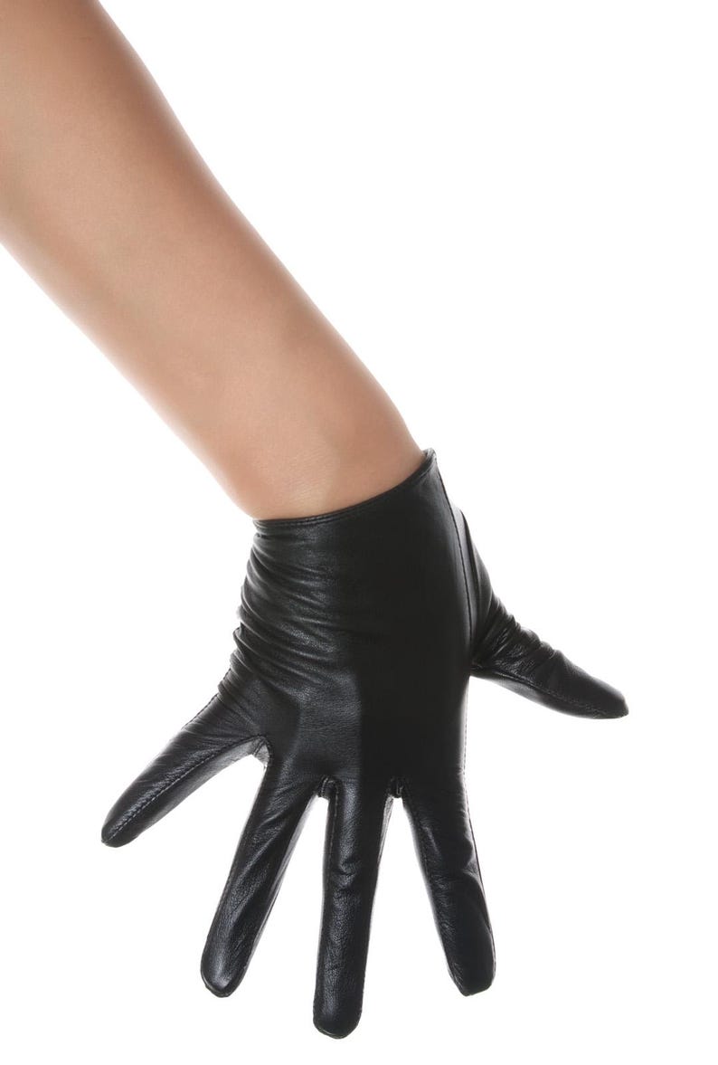 May include: A short black leather glove with a smooth finish and visible stitching along the fingers. The glove features a slightly gathered wrist area and extends to cover the palm and fingers, providing a sleek and fitted appearance on the hand.