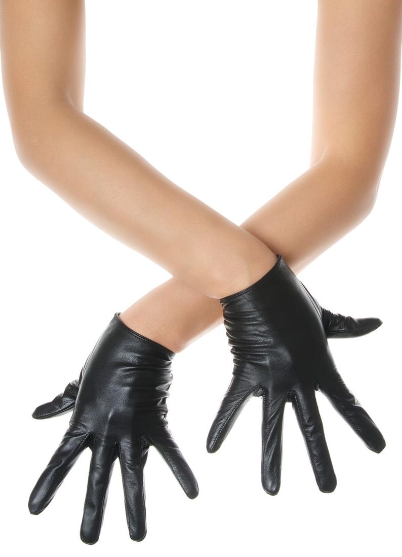 May include: A pair of black leather gloves with a smooth finish and a short wrist length. The gloves feature visible stitching along the fingers and a slightly gathered texture at the wrist area, providing a fitted appearance on the hands.