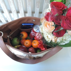 May include: A brown leather tote bag with a white fur lining. The bag is filled with fruit, a can of soda, and a cell phone. A bouquet of red and white roses is next to the bag.