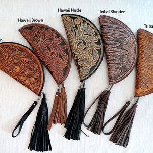 May include: Five half-moon shaped leather clutches with tassel accents. The clutches are decorated with different embossed patterns, including floral designs and feathers. The clutches are labeled "Hawaii Tan", "Hawaii Brown", "Hawaii Nude", "Tribal Blondie", and "Tribal Tan".