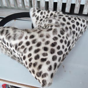 Puede incluir: Un bolso de mano con forma triangular que presenta un estampado animal en blanco y negro con un acabado texturizado similar al pelaje. El bolso incluye una correa negra s&oacute;lida que se curva a lo largo del borde superior, contrastando el dise&ntilde;o.