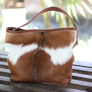 May include: A brown and white cowhide tote bag with a brown leather handle.