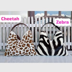 Puede incluir: Dos bolsos de estilo hobo con acabado de pelo texturizado. El bolso de la izquierda presenta un estampado de guepardo en marr&oacute;n y crema con asa marr&oacute;n. El de la derecha muestra un patr&oacute;n de rayas de cebra en blanco y negro con asa negra. Texto Cheetah y Zebra.