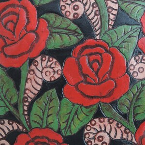 May include: Close-up of a black leather background with red roses and green leaves. The roses are painted on the leather and have a 3D effect.