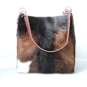 May include: A brown, black, and white cowhide tote bag with brown leather straps and silver hardware.
