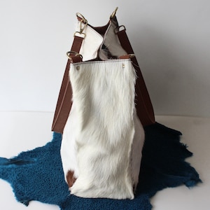 Puede incluir: Un bolso tote de cuero blanco y marr&oacute;n con correas largas. El bolso est&aacute; hecho de piel de vaca y tiene un patr&oacute;n &uacute;nico y natural.