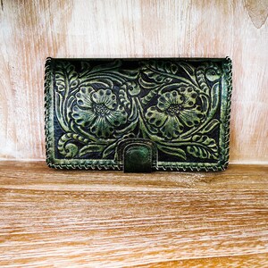 May include: A green leather wallet with a floral embossed design. The wallet has a stitched border and a small metal clasp.