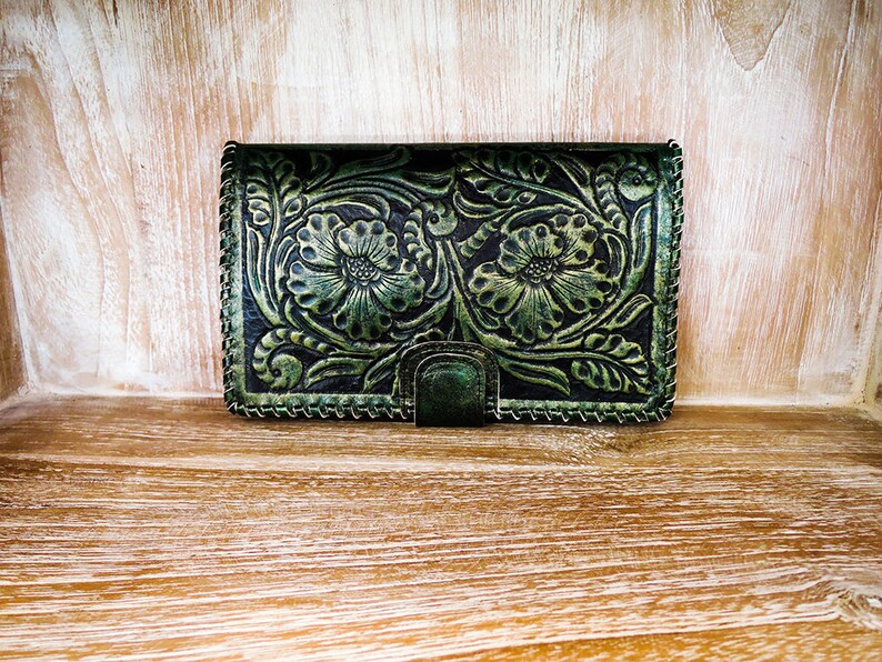 May include: A green leather wallet with a floral embossed design. The wallet has a stitched border and a small metal clasp.