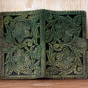 May include: A green leather journal with a floral embossed design. The journal has a stitched edge and a flap closure.
