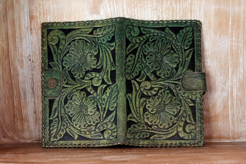 May include: A green leather journal with a floral embossed design. The journal has a stitched edge and a flap closure.