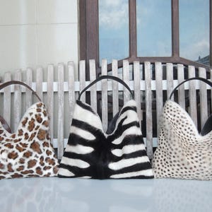 Puede incluir: Tres bolsos de mano estilo hobo con estampados inspirados en animales. El bolso de la izquierda tiene un estampado de leopardo marr&oacute;n y negro, el central un patr&oacute;n de rayas de cebra blanco y negro, y el de la derecha un dise&ntilde;o de puntos de guepardo.