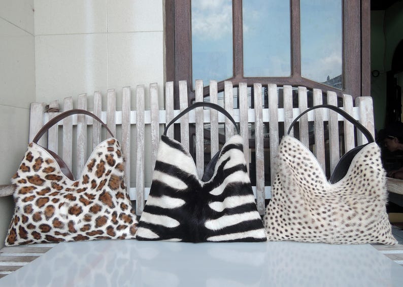 Puede incluir: Tres bolsos de mano estilo hobo con estampados inspirados en animales. El bolso de la izquierda tiene un estampado de leopardo marr&oacute;n y negro, el central un patr&oacute;n de rayas de cebra blanco y negro, y el de la derecha un dise&ntilde;o de puntos de guepardo.