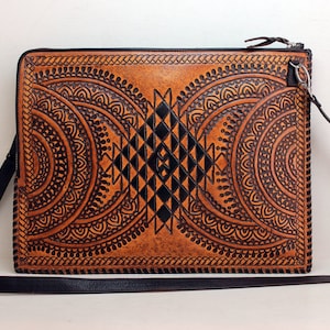 Puede incluir: Un bolso de cuero marrón con correa negra y diseños geométricos intrincados tallados en la parte delantera.