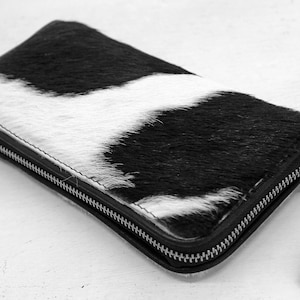 May include: A black and white cowhide wallet with a zipper closure and a black leather strap.