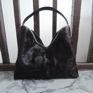 May include: A black leather handbag with a long strap. The bag is made of a soft, fuzzy material.