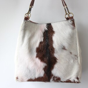 Puede incluir: Un bolso tote de piel de vaca blanca, marr&oacute;n y rosa con asas de cuero marr&oacute;n y herrajes dorados.