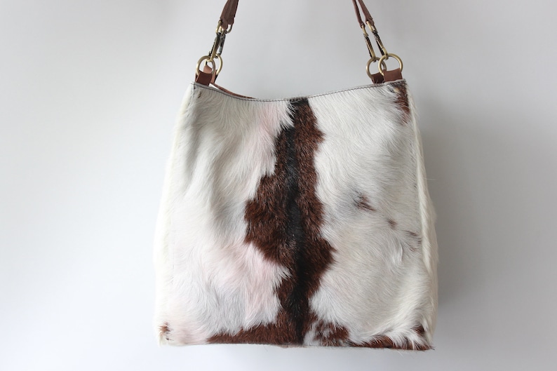 Puede incluir: Un bolso tote de piel de vaca blanca, marr&oacute;n y rosa con asas de cuero marr&oacute;n y herrajes dorados.